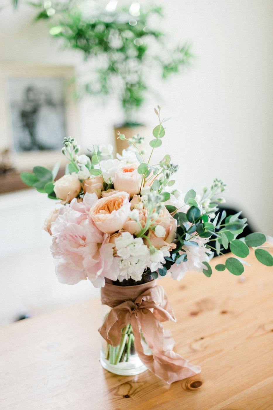 Soft pink roses and greenery gathered in a glass jar on a wooden table