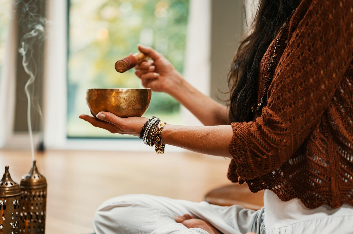 Hands holding a brass singing bowl beside a curl of incense smoke
