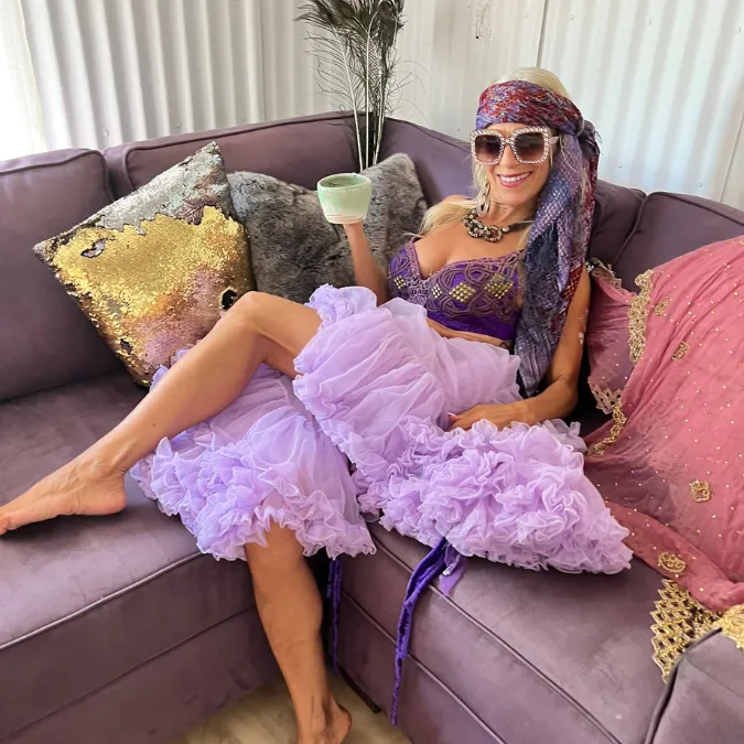 Staci relaxing on a mauve velvet sofa, raising a cup of tea and smiling